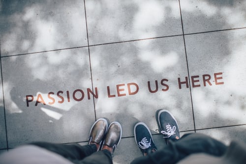 Overhead view of two pairs of feet standing near the text 'Passion Led Us Here' written on tiled pavement, symbolizing inspiration and purpose. Interview follow-up tips