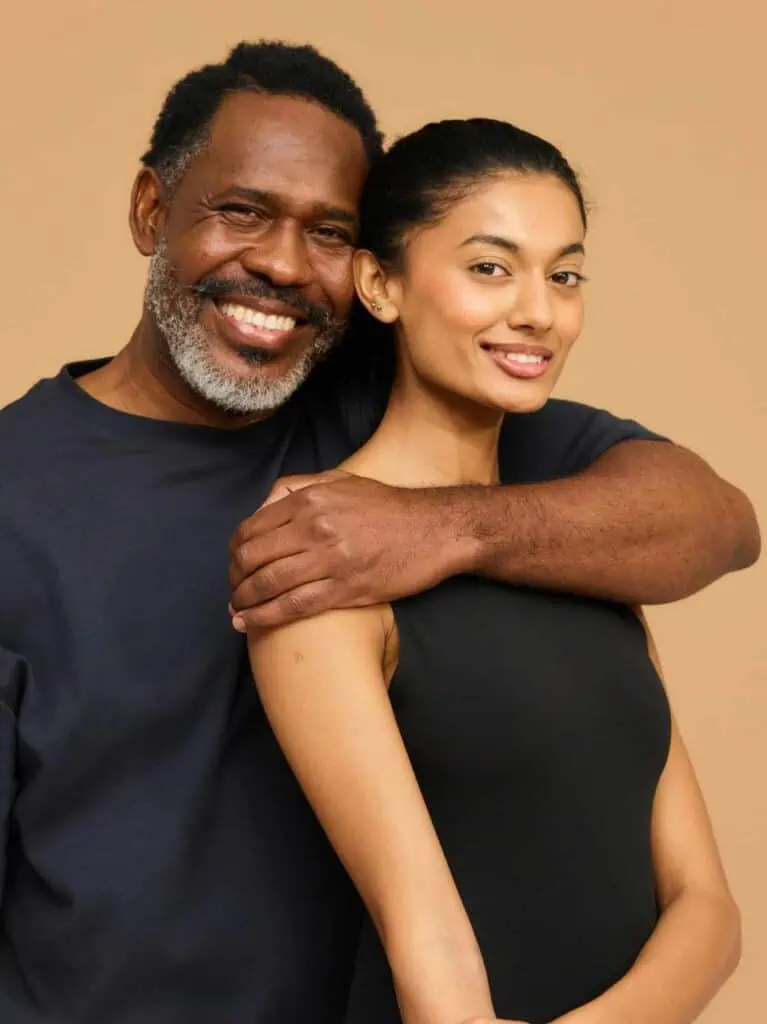A happy immigrant couple embracing and smiling against a neutral beige background, symbolizing love, partnership, and a shared journey.