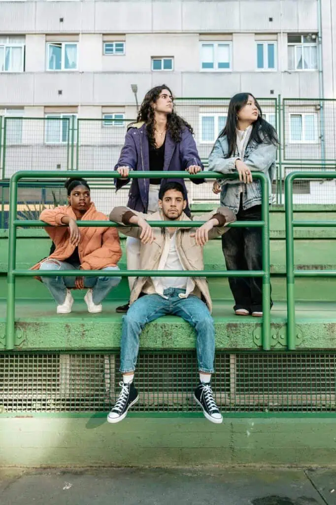 Four diverse young Australian immigrant students in casual clothing posing on green metal railings in an urban outdoor setting CV for Immigrants