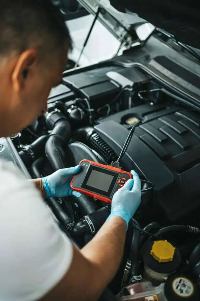 Automotive electrician diagnosing car engine using electronic diagnostic tool