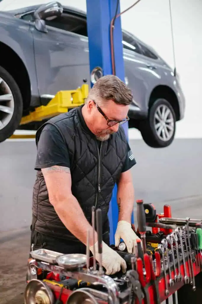 Automotive technician organizing tools at vehicle repair station with car lifted on hydraulic lift