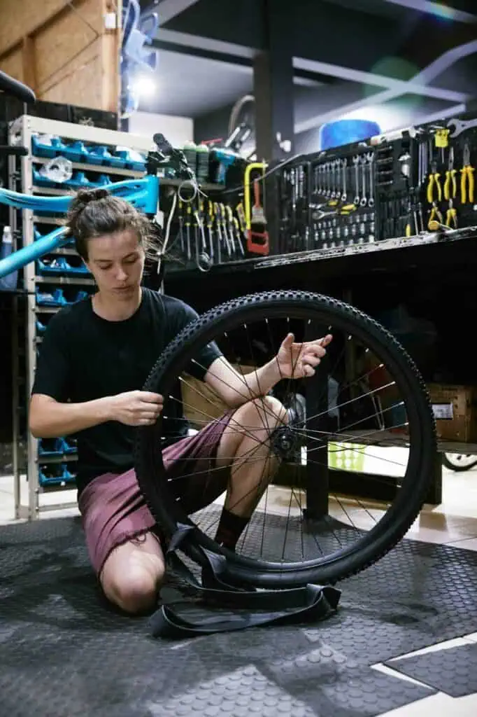 Bicycle technician repairing a bike wheel in a workshop filled with tools.