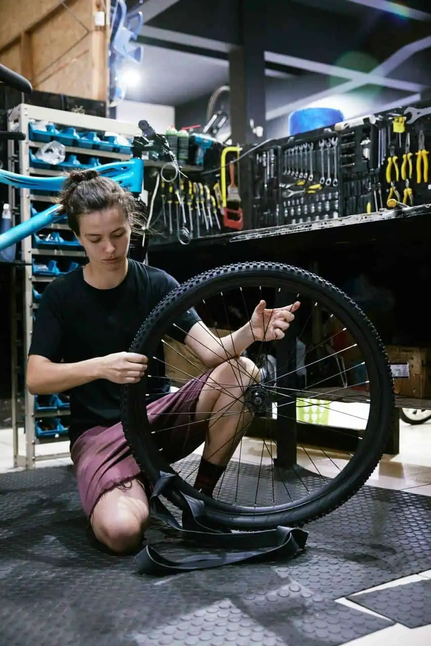 Bicycle technician repairing a bike wheel in a workshop filled with tools.