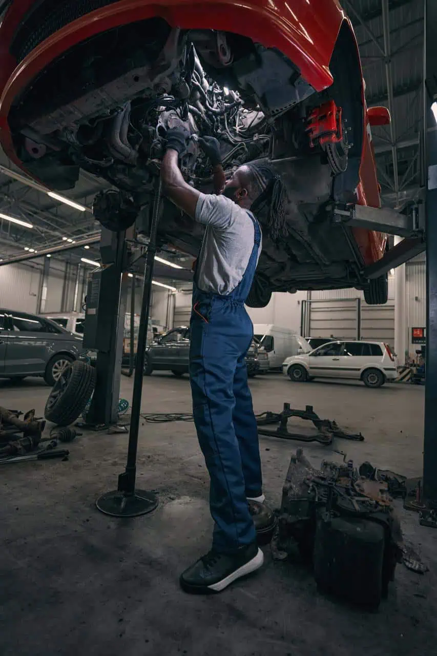 Brake and suspension technician working under elevated car in a professional garage