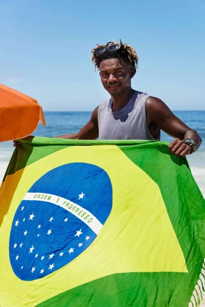 Smiling student on a Brazilian beach holding the national flag, representing education, travel, and career opportunities in Brazil.