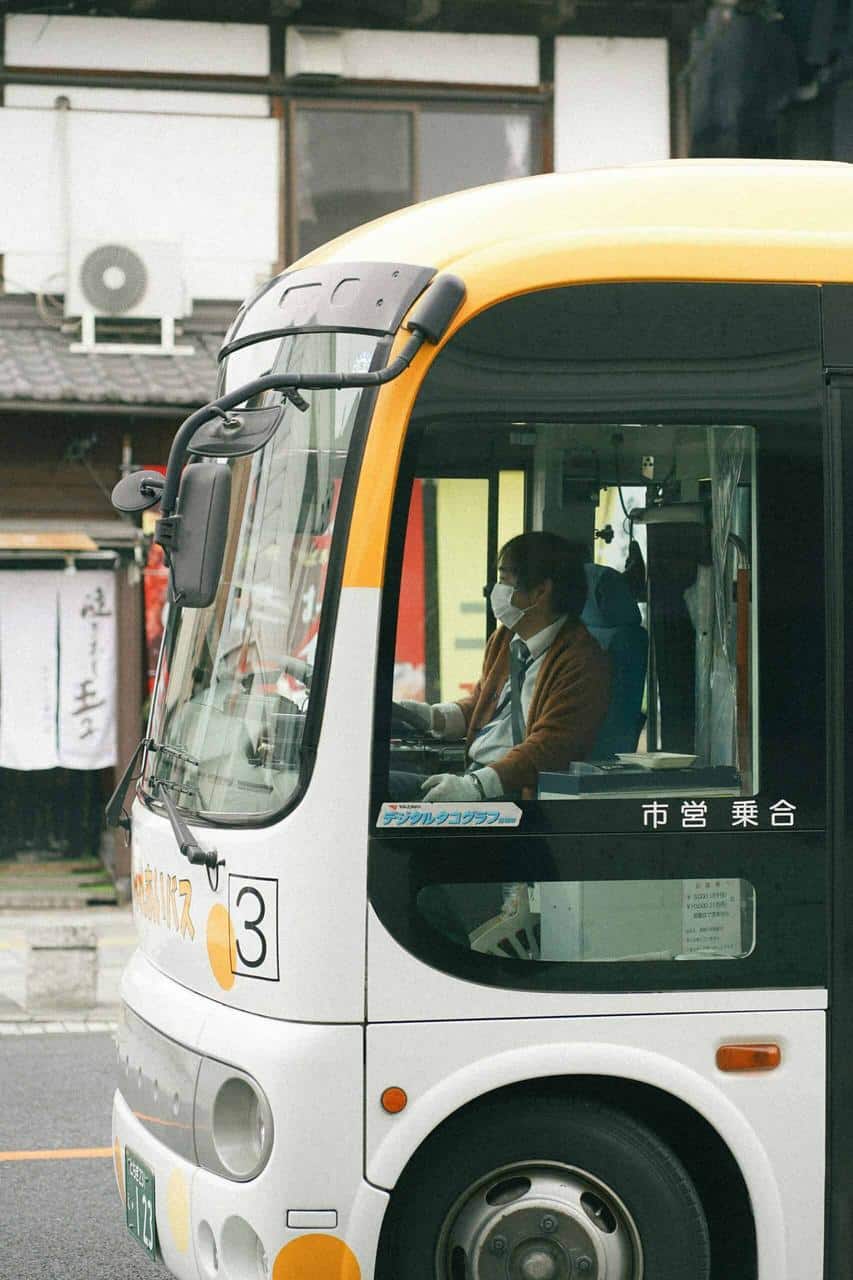 Professional bus driver wearing a mask while driving a public transport vehicle in an urban setting.