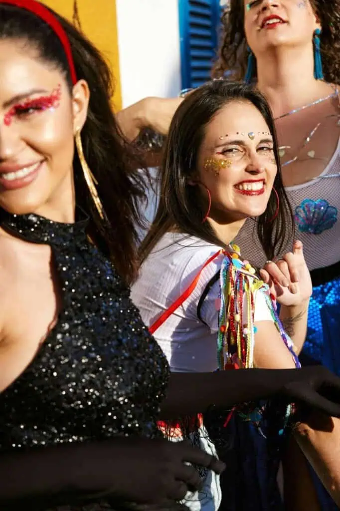 Close-up of Chilean women dressed in vibrant, glittery costumes and accessories, smiling and celebrating during a colorful Carnival parade.