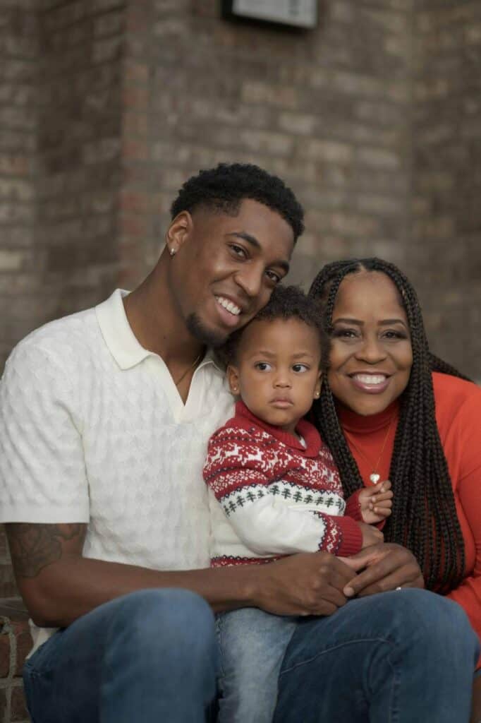 Smiling Columbian family of three, including a father, mother, and toddler, sitting together on steps in festive attire with a brick wall in the background talking about CV for Immigrants and Students.