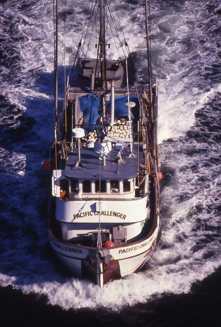 A commercial fishing vessel named 'Pacific Challenger' navigating through ocean waters, carrying equipment and fresh catch.