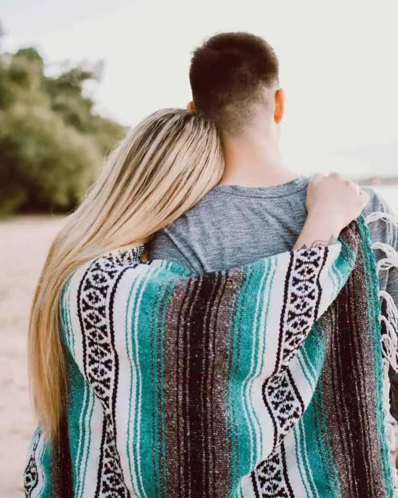 A couple embracing outdoors, wrapped in a patterned blanket, symbolizing connection and comfort.