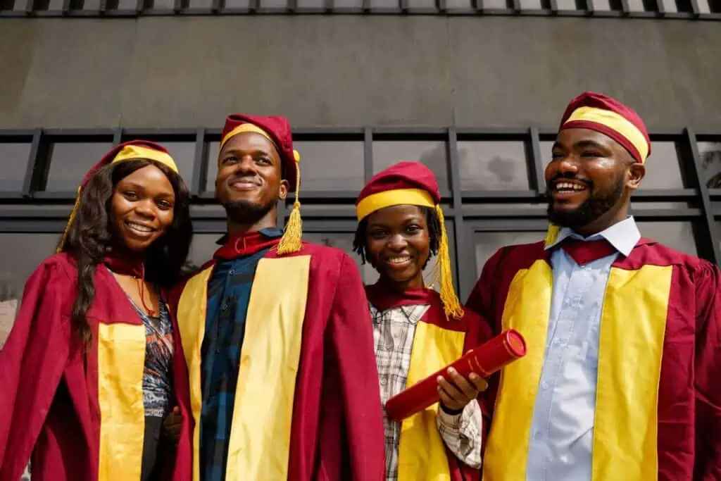 Four Ethiopian tertiary graduates in maroon and yellow academic gowns celebrating their achievement outdoors with bright smiles