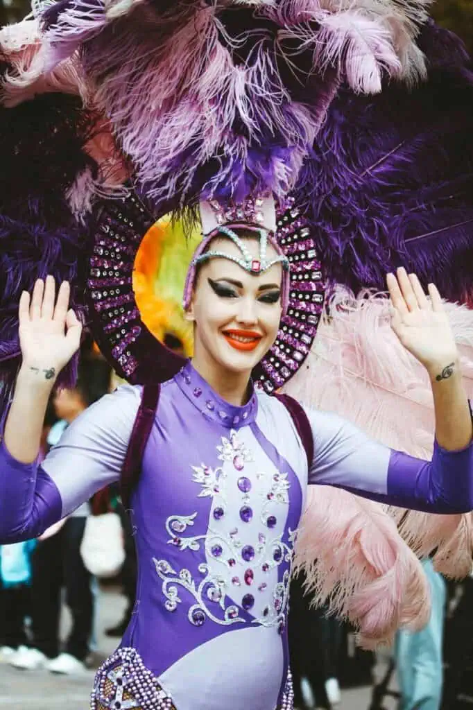 Smiling festival performer in a vibrant purple costume with feathers, celebrating culture, travel, and student experiences
