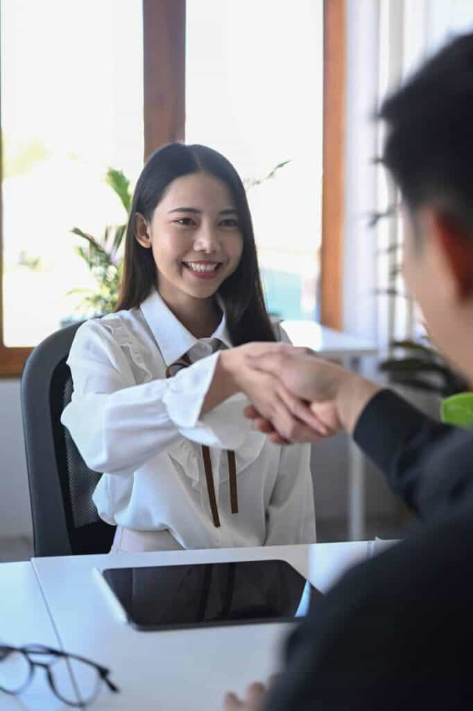 Happy young professional shaking hands with an employer after receiving a job offer in a modern office setting.