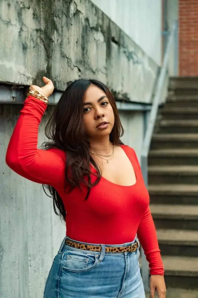 A young Guatemalan woman in a bold red top and denim jeans standing near an urban staircase, exuding confidence as she prepares to start a new chapter in her life.