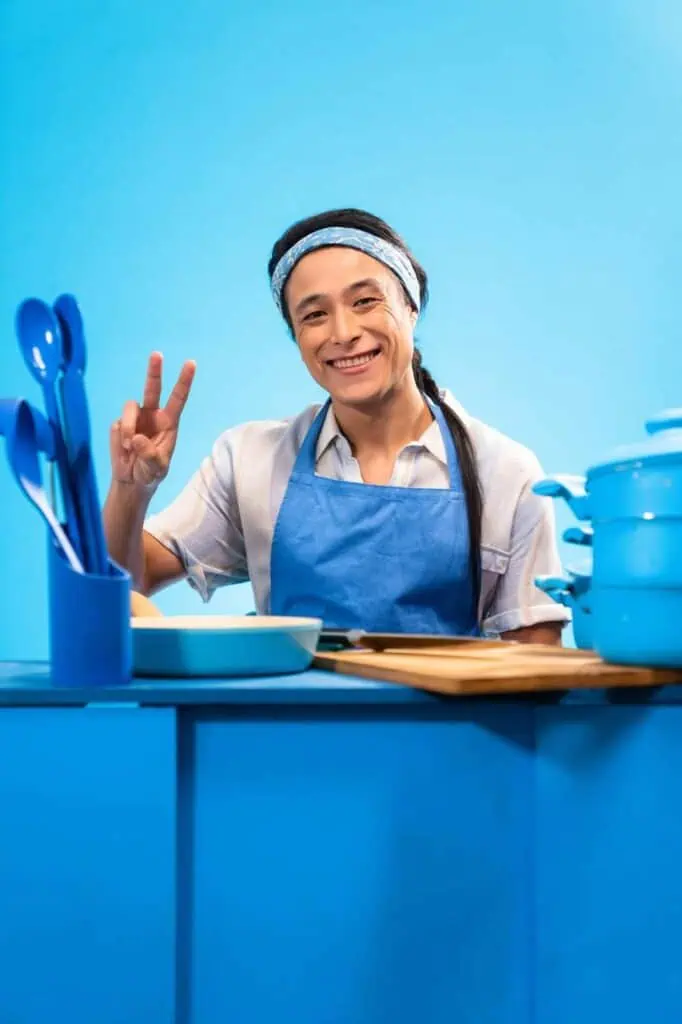 Hospitality tutor in apron smiling at kitchen counter with cookware
