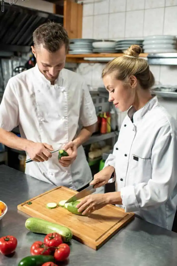 Two professional chefs preparing fresh ingredients in a restaurant kitchen, showcasing teamwork and career opportunities in hospitality and culinary arts.