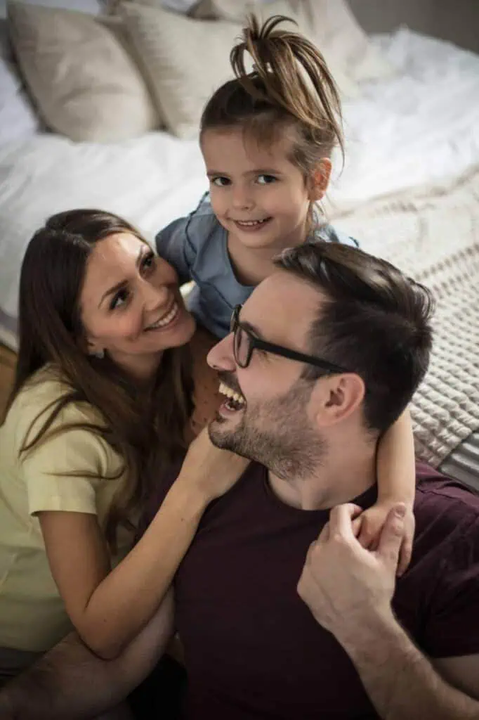 Happy immigrant family, including a father, mother, and daughter, sharing a joyful moment together in a cozy bedroom as they prepare for their move to Germany.