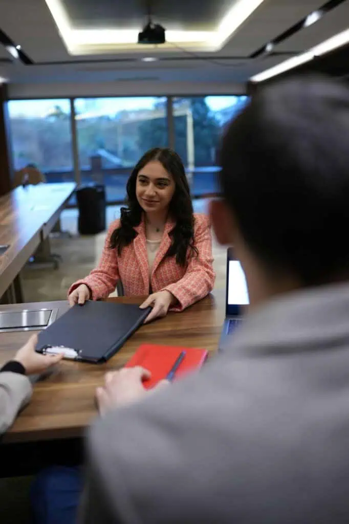 Confident young woman handing over her resume during a job interview in a modern office setting.