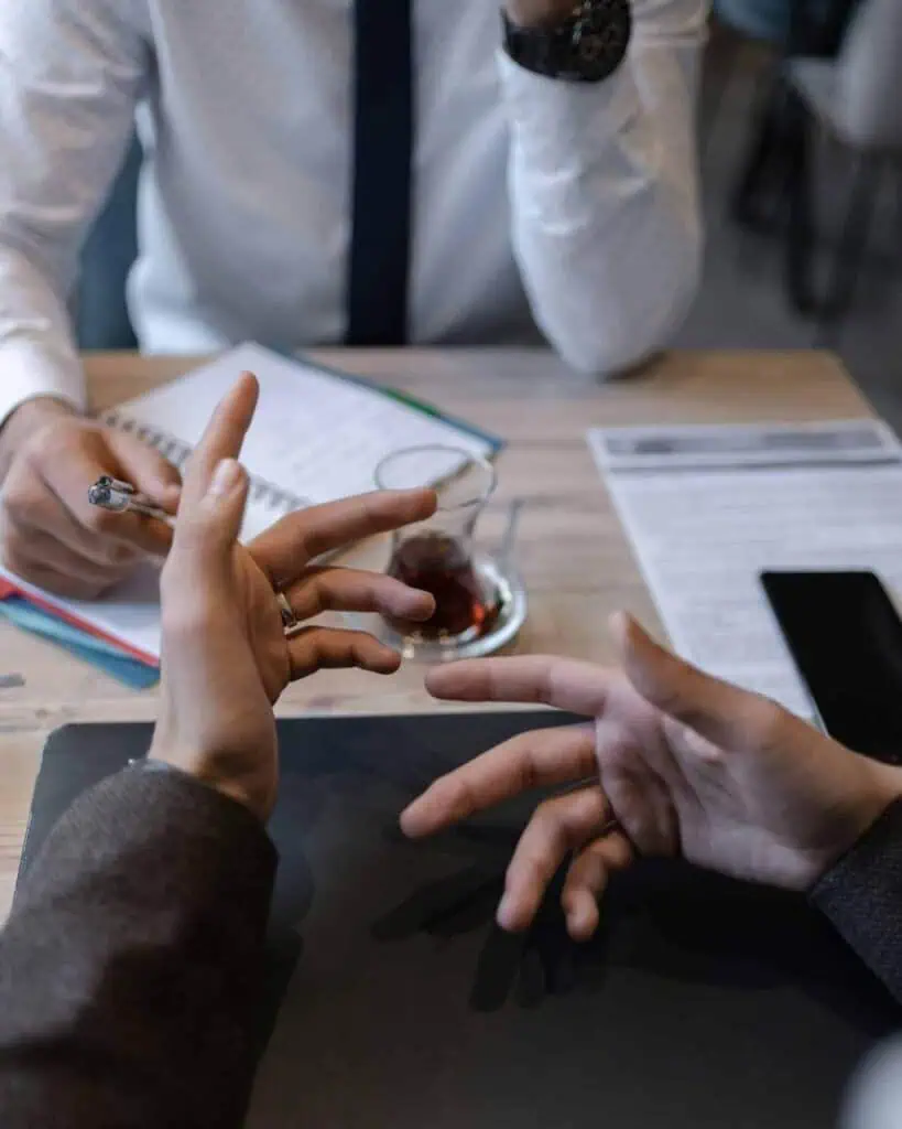 Close-up of hands negotiating a job offer over a table with documents, a pen, and tea in a professional setting.