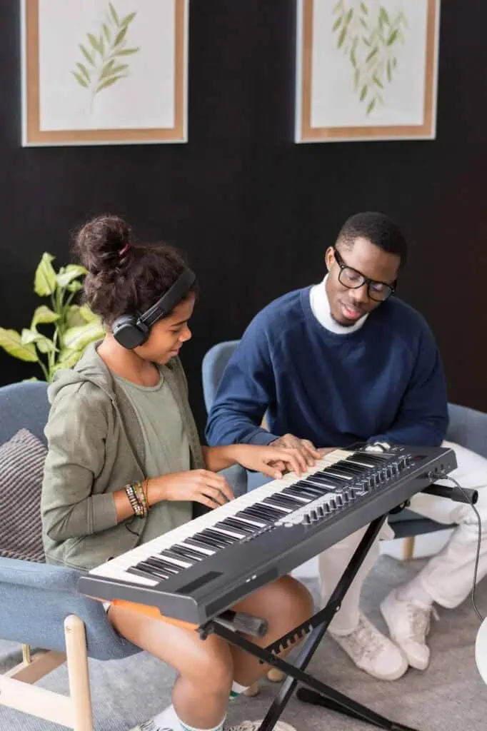 A music teacher guides a young student playing an electronic keyboard during a private lesson; the student wears headphones.