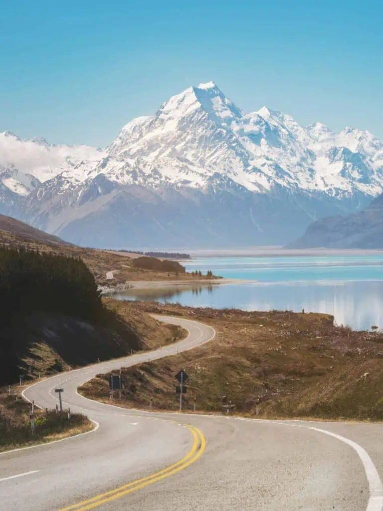 Scenic winding road leading to snow-capped mountains and a crystal-clear lake in New Zealand, symbolizing adventure, career growth, and study opportunities.