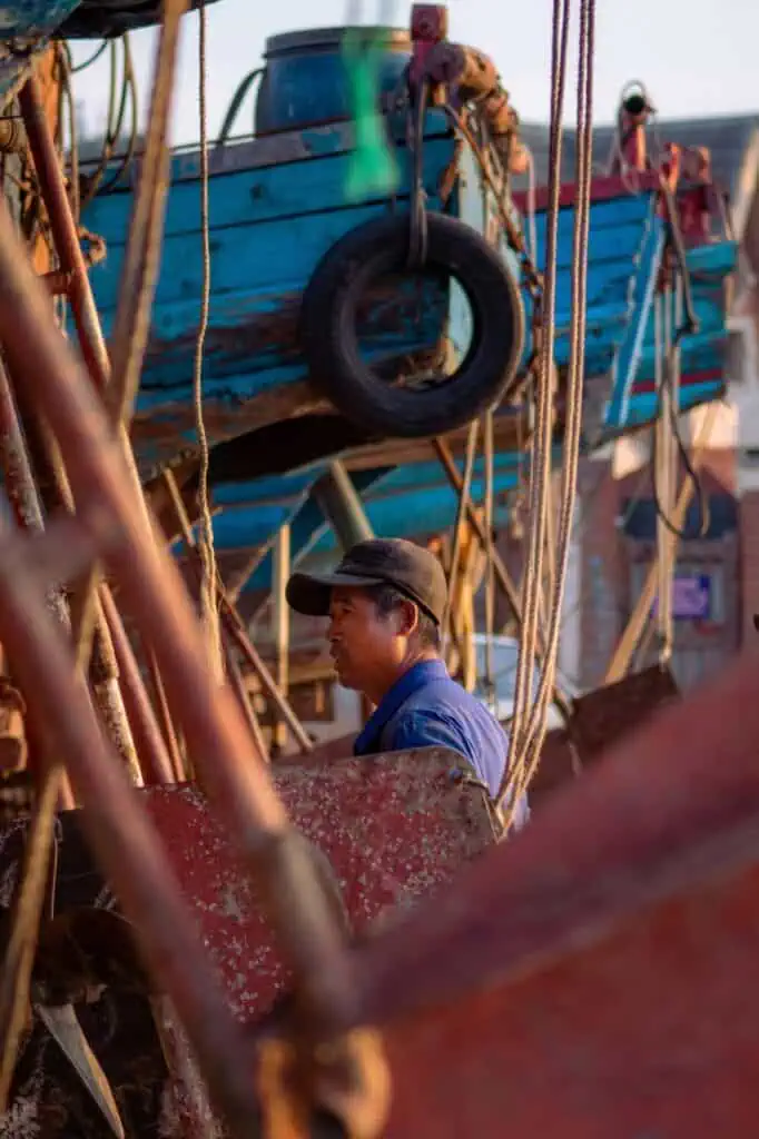 Ordinary seaman on deck near fishing boats performing maintenance tasks