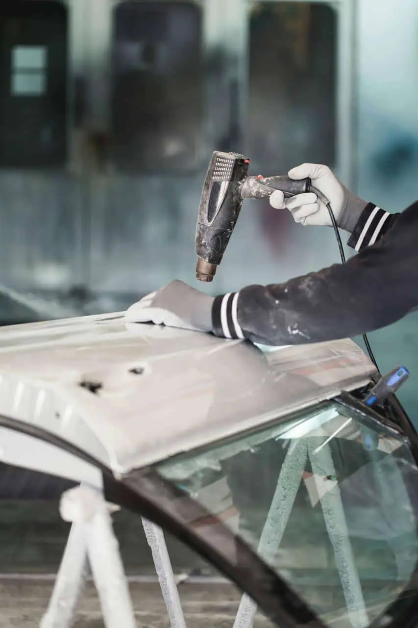 Auto body technician using heat gun on vehicle panel for collision repair.