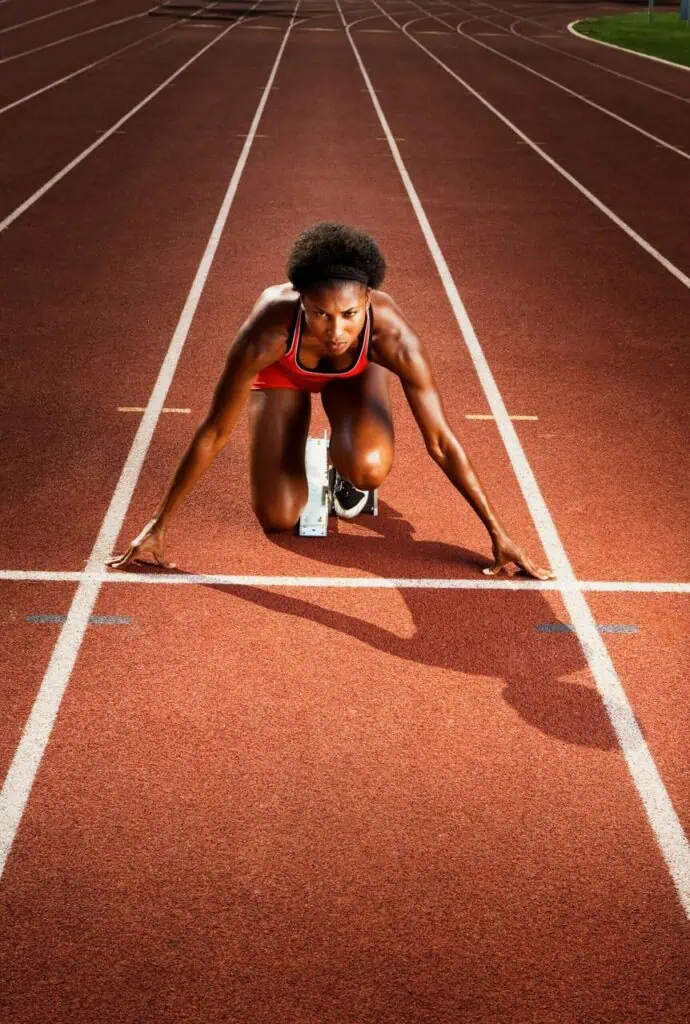 Female track athlete in a red uniform prepares to sprint from the starting blocks on a professional running track.