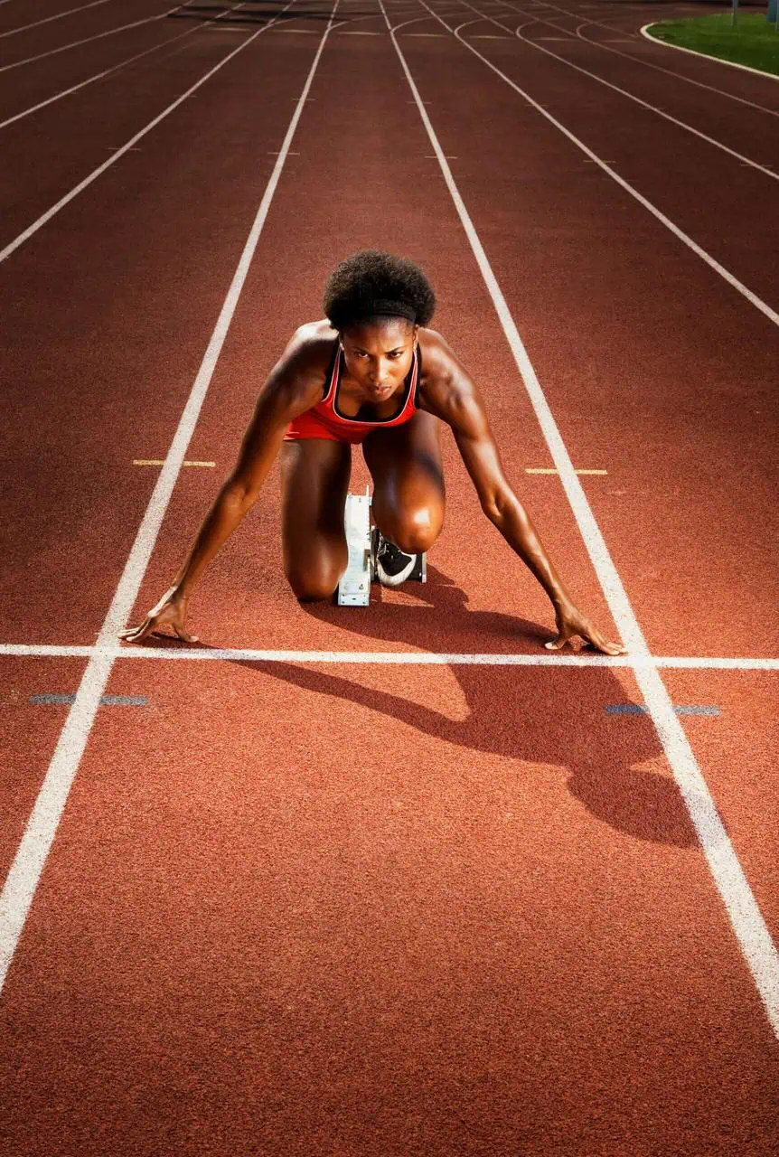 Female track athlete in a red uniform prepares to sprint from the starting blocks on a professional running track.