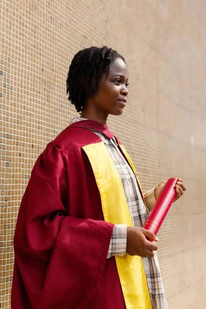 A proud Nigerian graduate in a maroon and yellow gown holding a diploma, ready to take the next step with a professionally written resume.