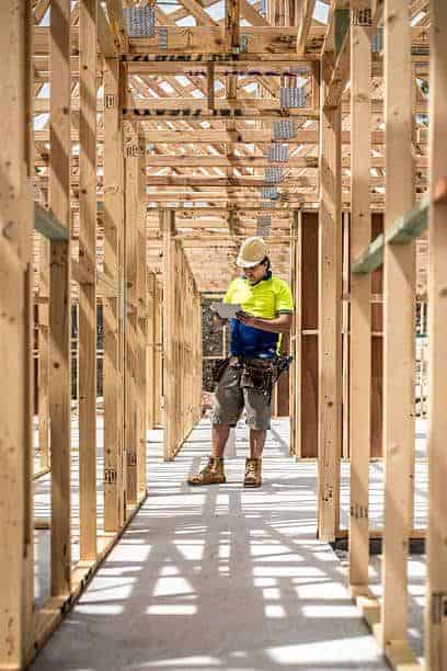 A construction worker inspecting a wooden building framework, highlighting career opportunities in property services, construction, and real estate development.