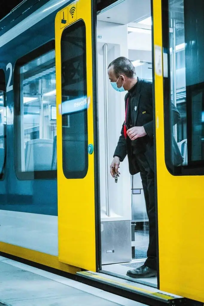 Railway conductor checking train platform while wearing uniform and face mask.