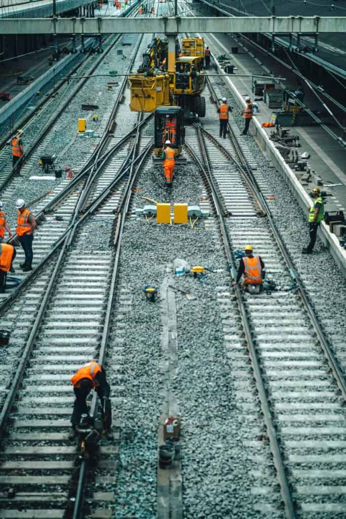 Railway maintenance workers in high-visibility gear repairing train tracks using heavy equipment