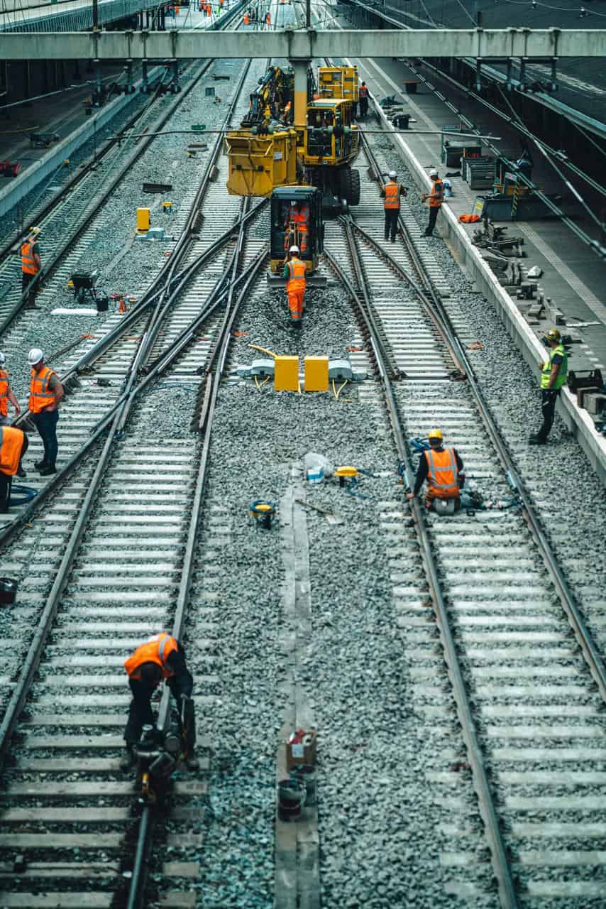Railway maintenance workers in high-visibility gear repairing train tracks using heavy equipment