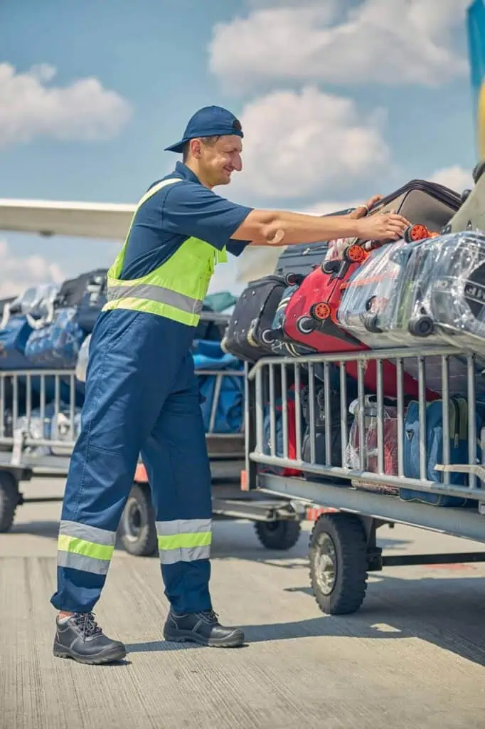 Ramp agent loading luggage onto airport baggage cart on tarmac