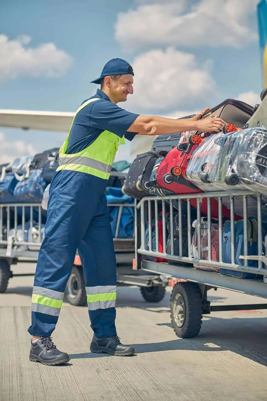 Ramp agent loading luggage onto airport baggage cart on tarmac