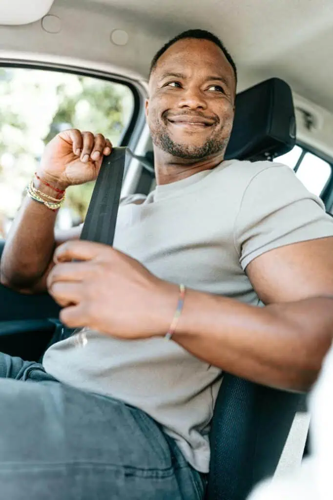 A smiling rideshare driver fastening his seatbelt, ready to start his shift with Uber or Lyft.