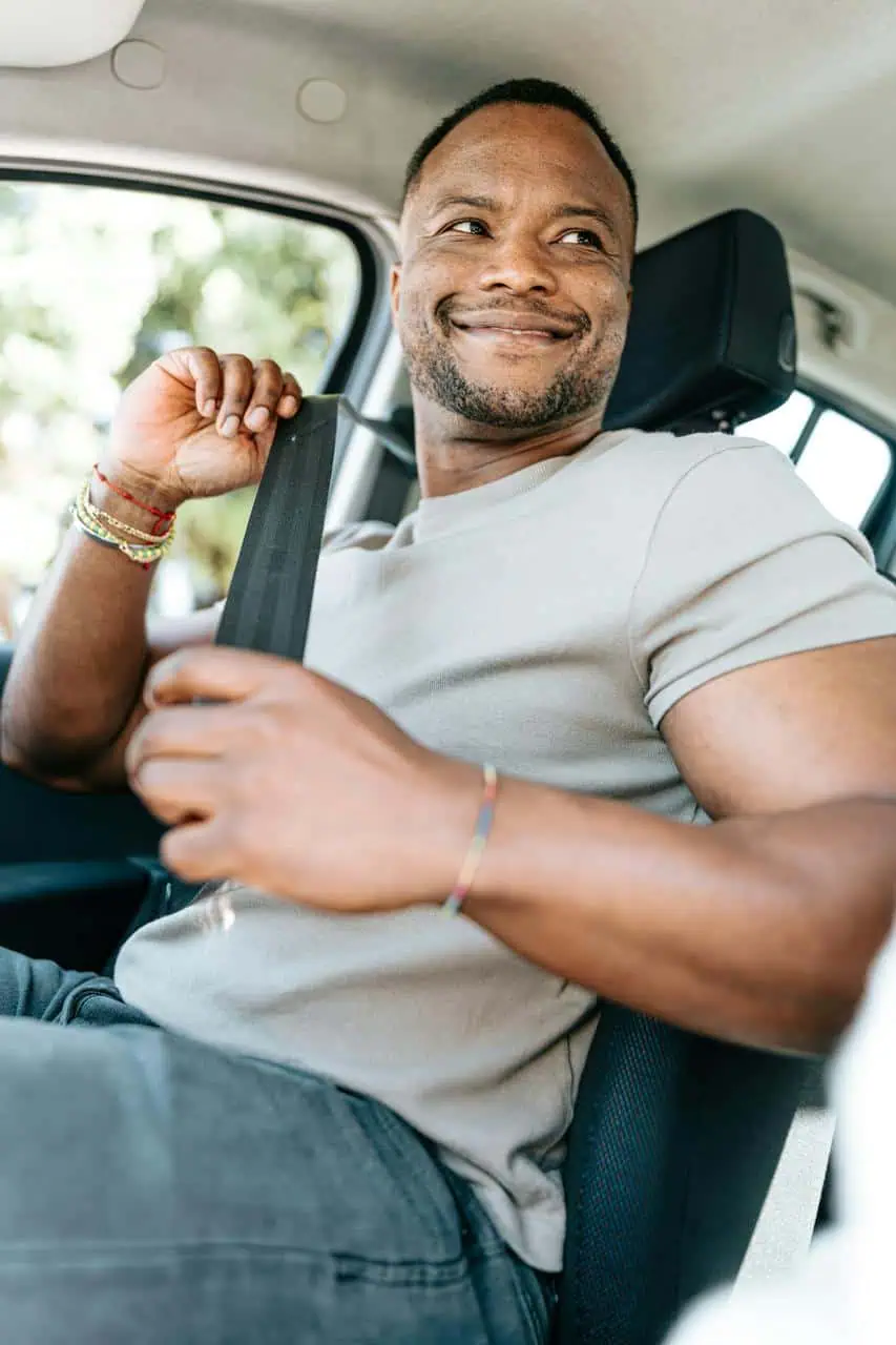 A smiling rideshare driver fastening his seatbelt, ready to start his shift with Uber or Lyft.