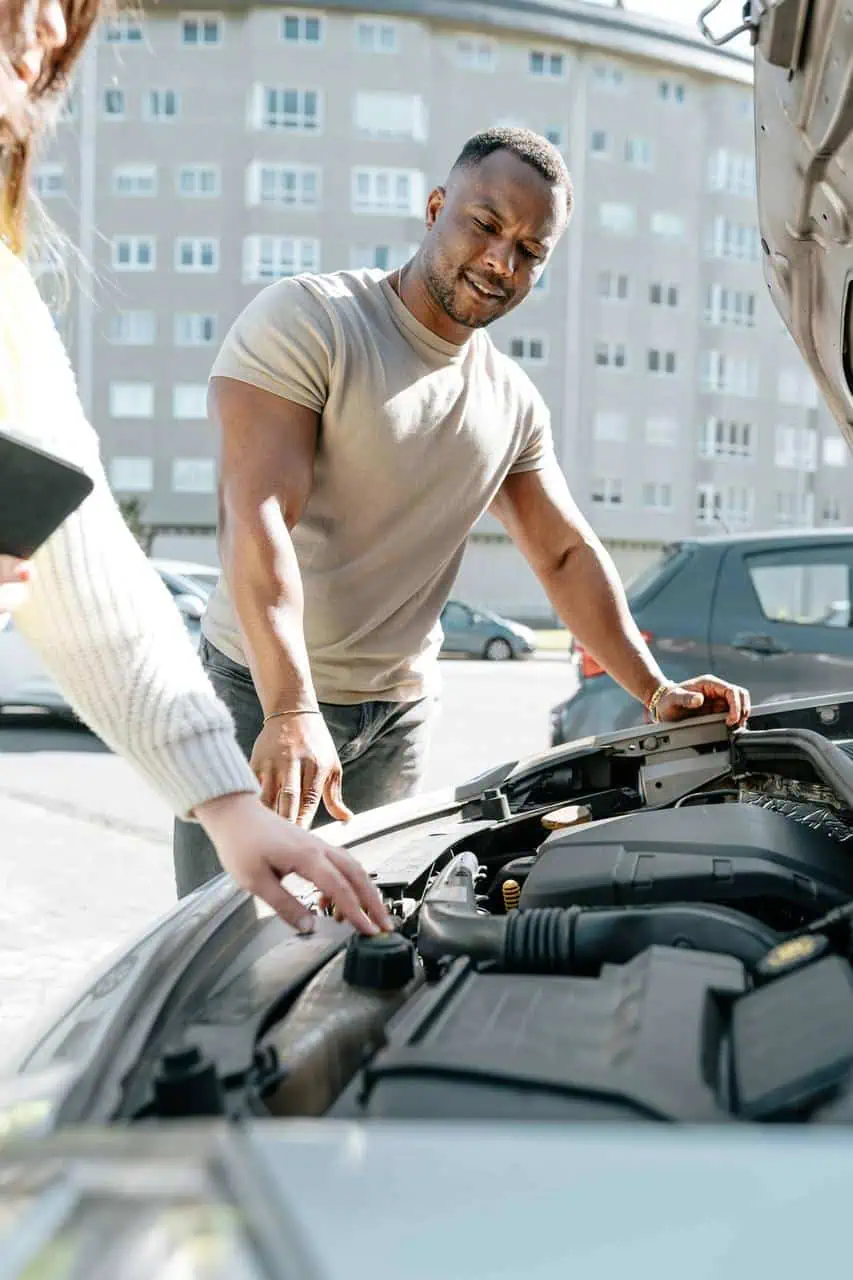 Roadside assistance technician inspecting a car engine while helping a driver on the roadside.