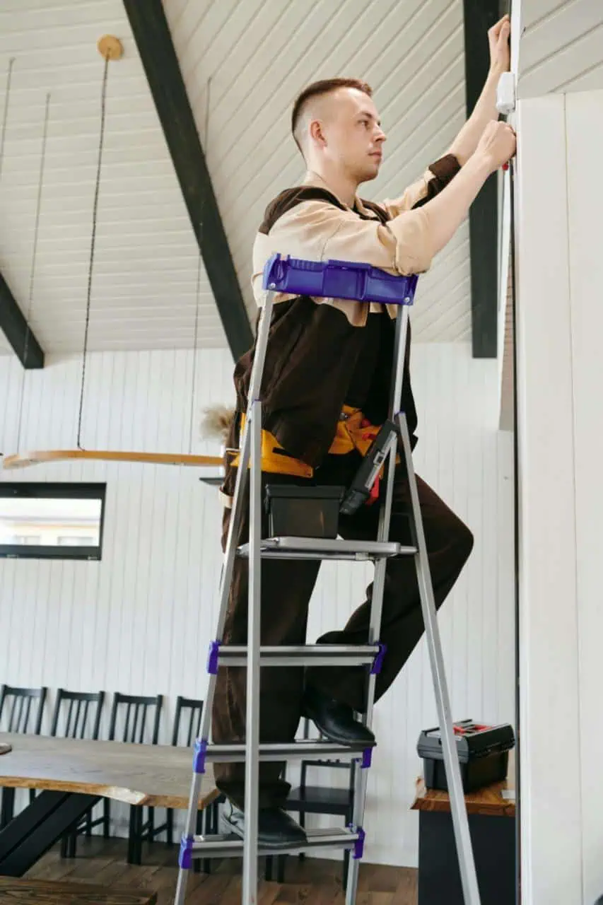 School caretaker performing maintenance work on a ladder inside an educational facility