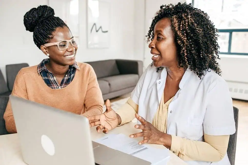 Student and advisor having a productive discussion during an academic interview, with a laptop and documents on the table in a bright office setting.