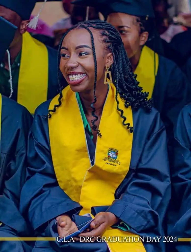 Smiling female graduate wearing a navy graduation gown and a yellow sash, celebrating during the C.L.A.-DRC Graduation Day 2024 ceremony.