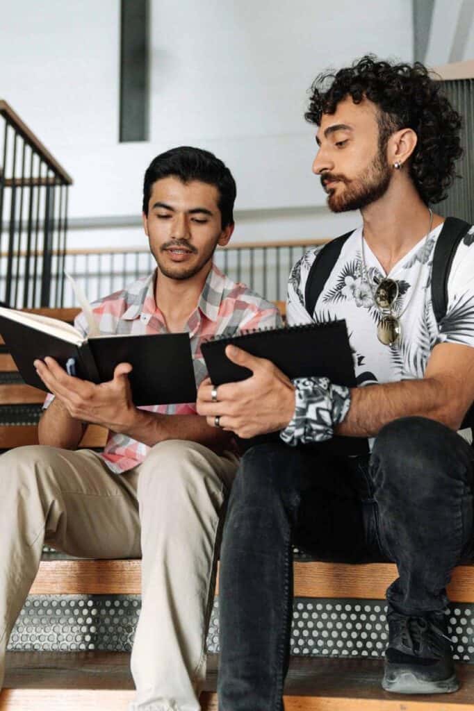Two young men sitting on stairs, reviewing notes and practicing interview questions together.