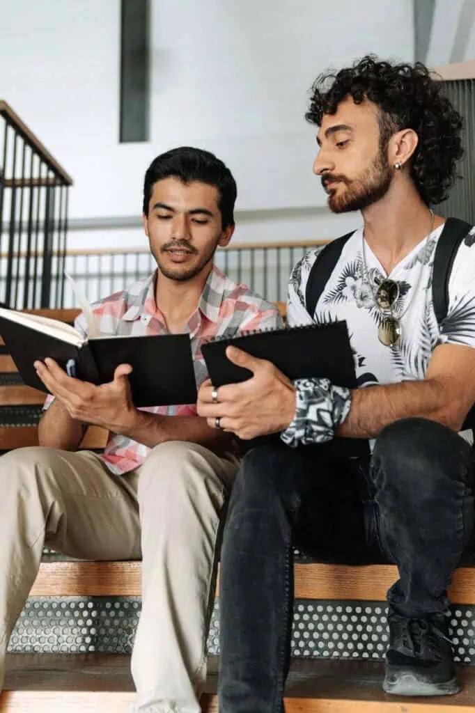 Two young men sitting on stairs, reviewing notes and practicing interview questions together.