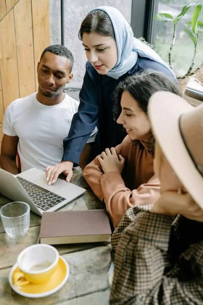 Diverse group of students collaborating on a laptop in a café, discussing study and work opportunities in Algeria.