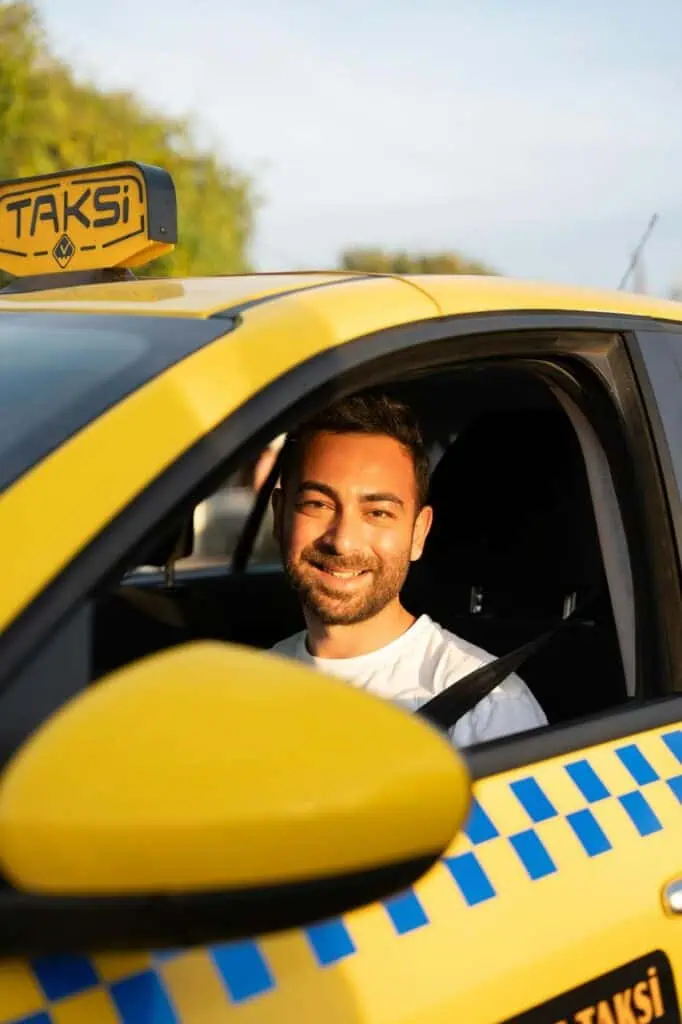 Smiling taxi driver sitting in a yellow cab, ready for work in the city.