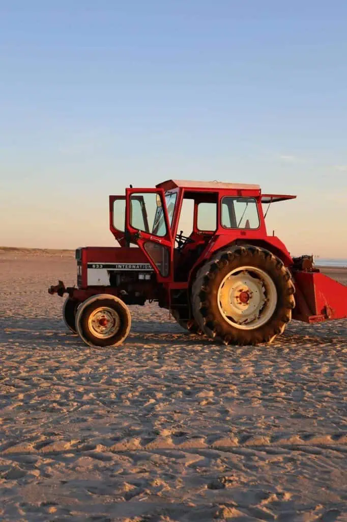A red tractor parked on a sandy field during sunset, representing career opportunities as a tractor operator in agriculture and land management.