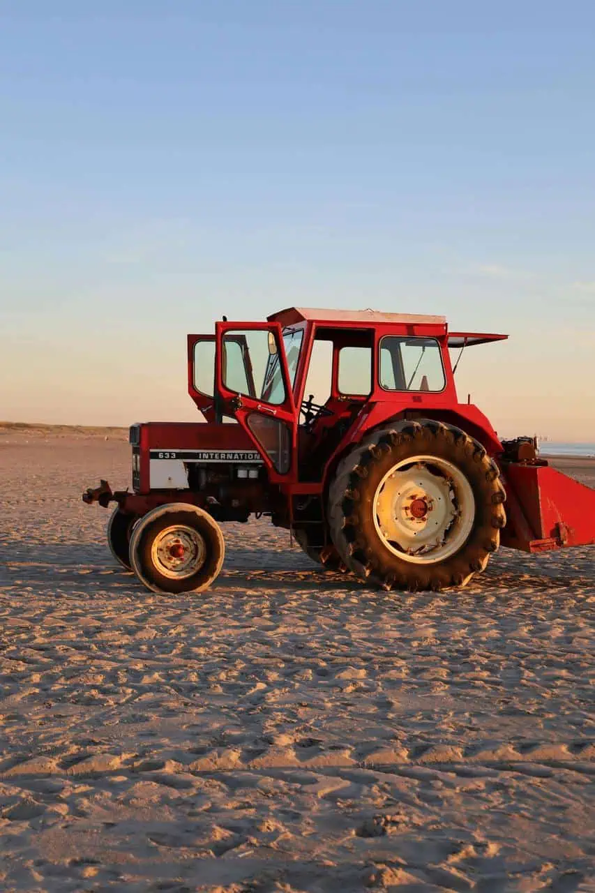 A red tractor parked on a sandy field during sunset, representing career opportunities as a tractor operator in agriculture and land management.