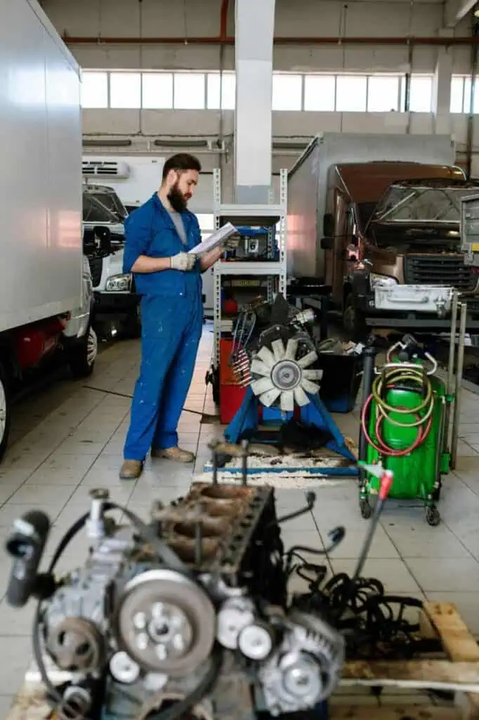 Truck mechanic inspecting repair manual in garage with truck engines and parts