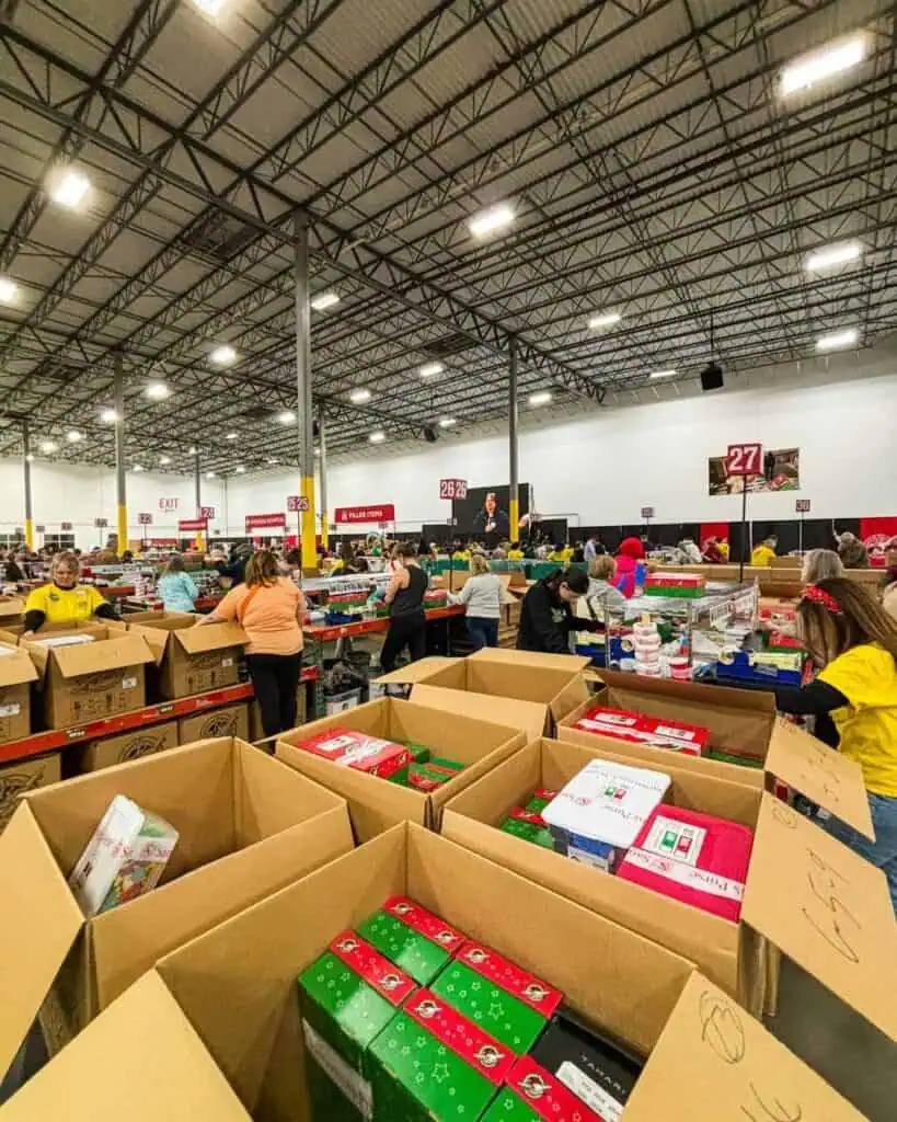 Volunteers sorting gift boxes in a large warehouse during a community outreach event.